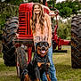 Atlas is registered to the contest to win money with this photo: girl, dog, rottweiler, tractor, grass, outdoor, smiling, animal, pet, nature, greenery, field, happy, casual_clothing, jeans, tank_top, daylight, portrait, farm, tree