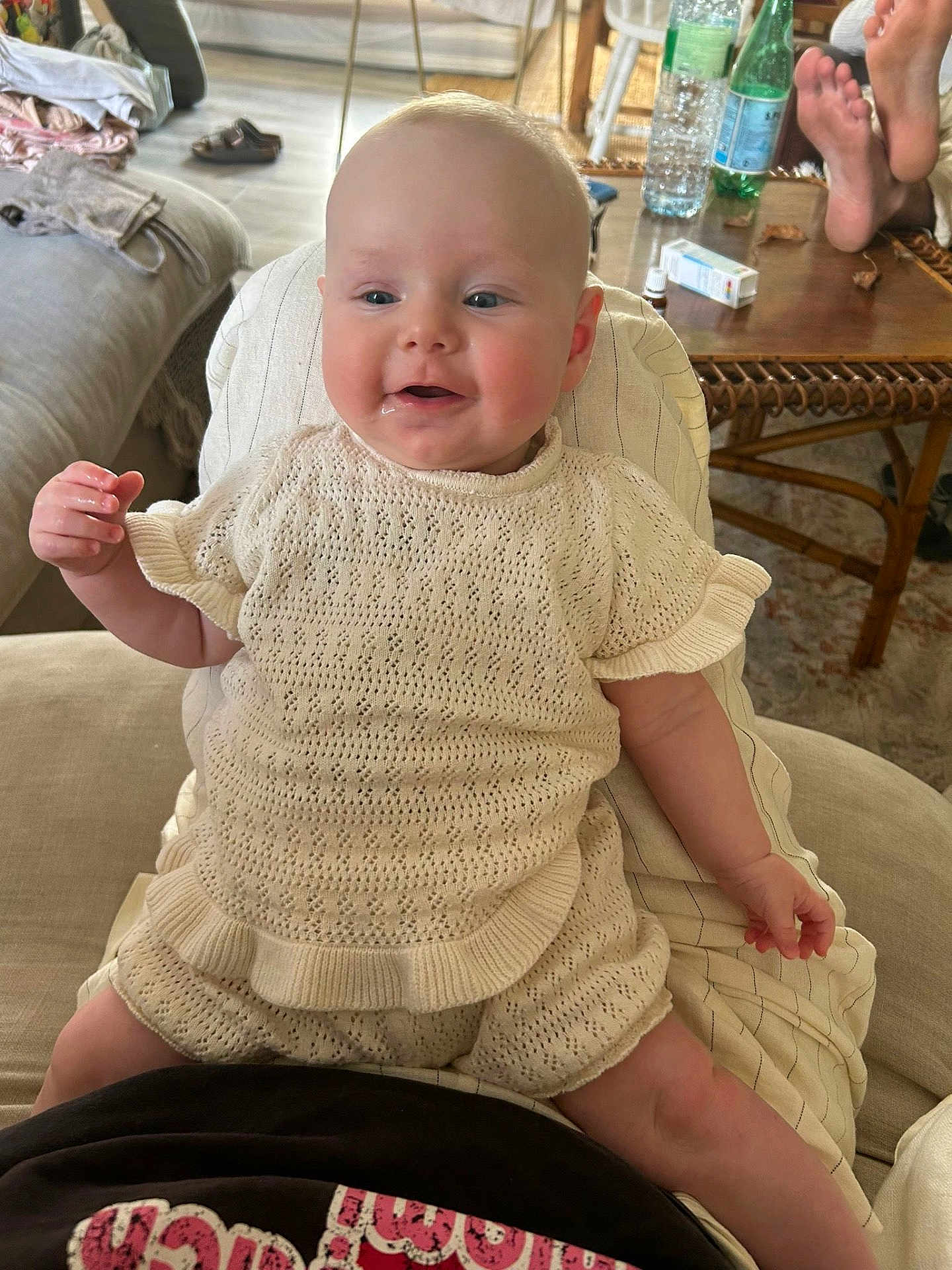 Jeanne a rejoint le concours — aidez-le/la à gagner de superbes lots ! baby, child, infant, knit_clothing, drool, smile, sitting, person, indoor, living_room, table, water_bottle, foot, barefoot, couch, blanket, relaxed, casual, home, happy