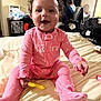 Kali joined the competition — help win amazing prizes! baby, child, pink_onesie, smiling, sitting, bed, toy, indoor, person, face, hair, polka_dot, furniture, background, window, curtain, adult, chair, television, household_items