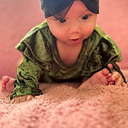 Kali is registered to the contest to win money with this photo: baby, infant, green_clothing, headband, black_headband, pink_blanket, soft_texture, curious_expression, indoor, close_up, face, hands, feet, child, crawling, portrait, cute, young, baby_girl, soft_lighting