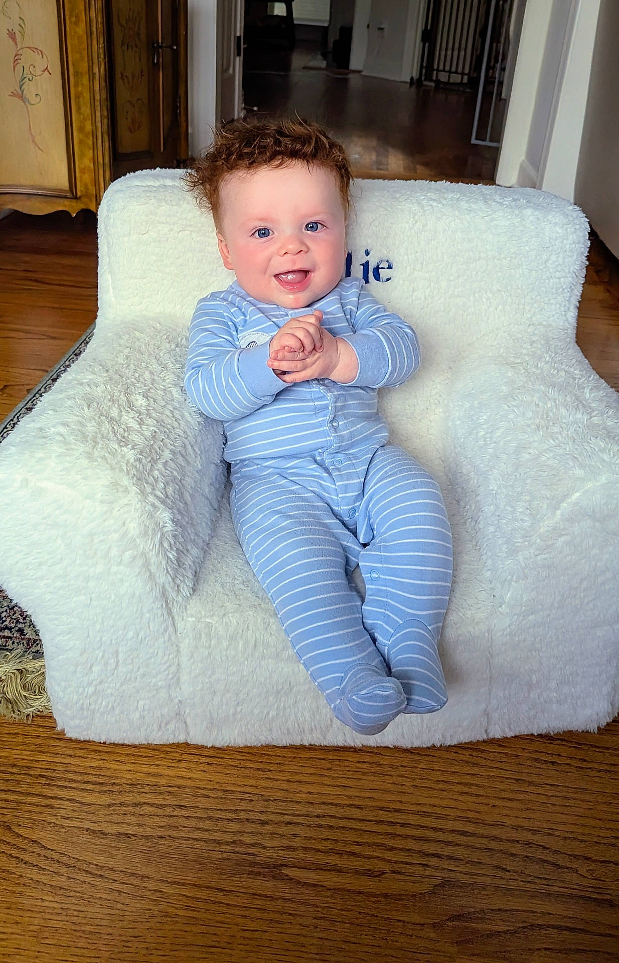 Matthew is registered to the contest to win money with this photo: armchair, baby, blue_eyes, child, clapping_hands, cozy, curly_hair, cute, furniture, happy, home, indoor, infant, pajamas, portrait, sitting, smiling, striped_clothing, white_fabric, wooden_floor