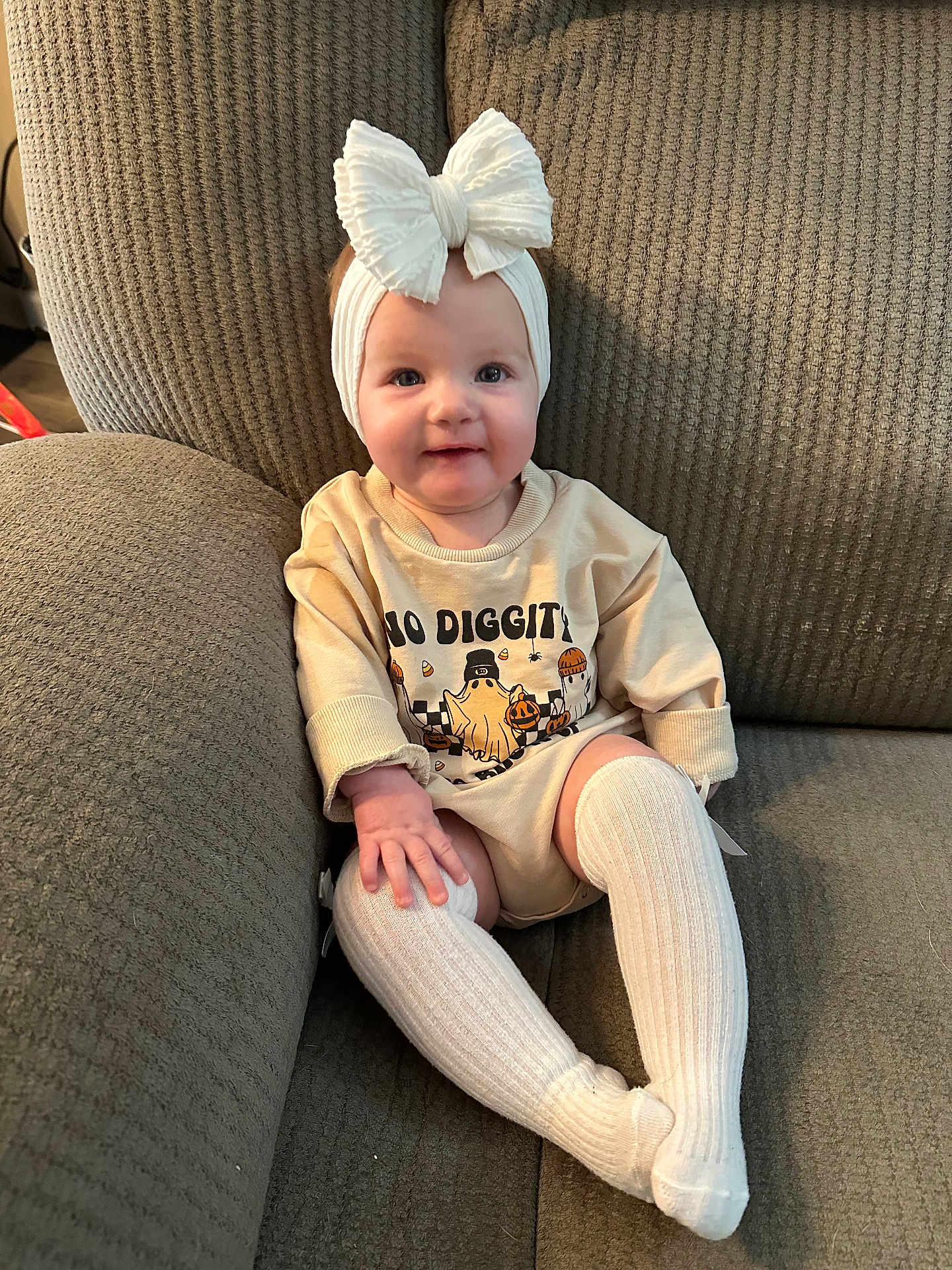 Paisley is registered to the contest to win money with this photo: baby, child, bow, headband, socks, couch, smile, clothing, infant, person, sitting, cute, happy, indoors, portrait, textile, knitwear, young_child, fashion, cozy
