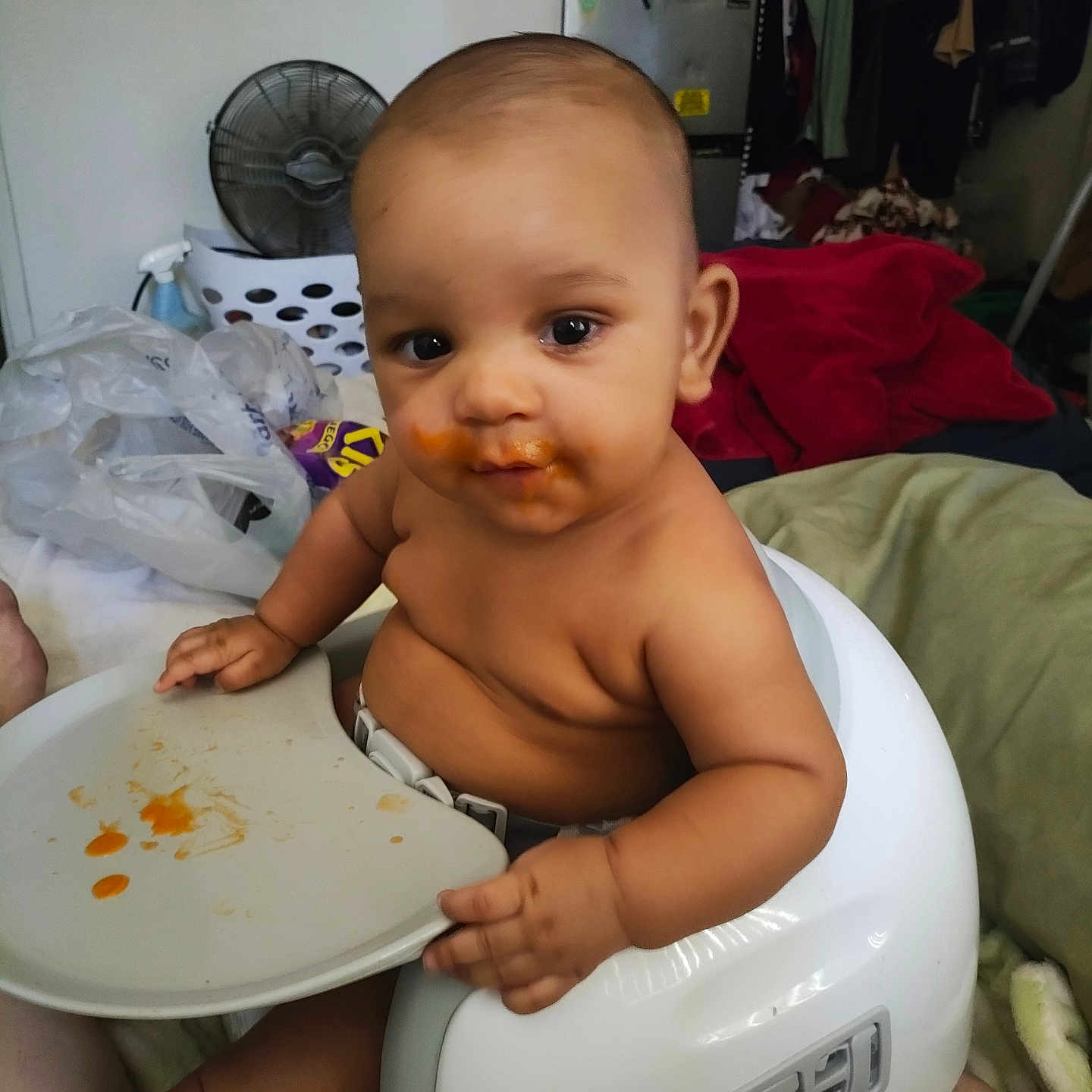 Tyrell is registered to the contest to win money with this photo: baby, blanket, child, clothing, clutter, expression, face, fan, food, foot, hand, highchair, indoor, messy, person, plastic_bag, refrigerator, seat, skin, tray