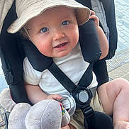 Milo-Chrisopher joined the competition — help win amazing prizes! baby, blue_eyes, bucket_hat, stroller, plush_toy, smiling, child, face, safety_harness, outdoor, cute, infant, clothing, hand, foot, seat, toy, daylight, happy, person