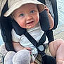 baby, blue_eyes, bucket_hat, stroller, plush_toy, smiling, child, face, safety_harness, outdoor, cute, infant, clothing, hand, foot, seat, toy, daylight, happy, person