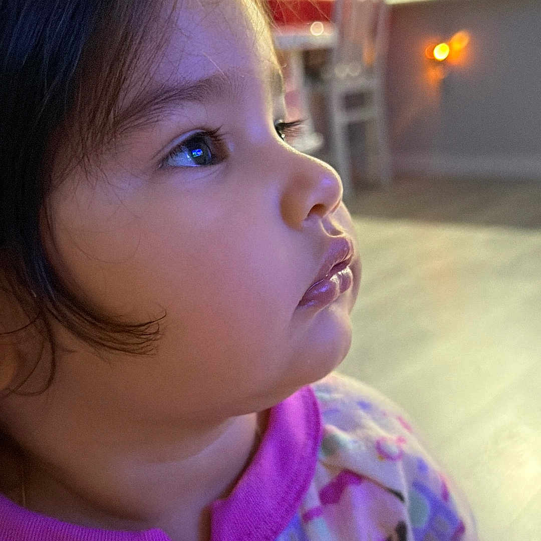 Caridad is registered to the contest to win money with this photo: blurred_background, chair, child, clothing, colorful, curly_hair, expression, face, floor, home, indoor, looking, onesie, person, profile, soft_lighting, toddler, toy_pattern, young_child, zipper