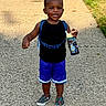 Marlon is registered to the contest to win money with this photo: child, toddler, smiling, outdoors, path, backpack, water_bottle, shorts, shirt, sneakers, standing, portrait, grass, sunlight, playful, happy, walking, pavement, summer, daylight