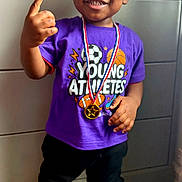 Marlon is registered to the contest to win money with this photo: child, toddler, boy, portrait, smiling, sports, athlete, medal, champion, victory, number_one, purple_shirt, basketball, soccer_ball, sneakers, black_pants, indoors, dresser, standing, happy