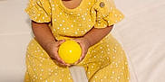 Juliette joined the competition — help win amazing prizes! toddler, child, yellow_outfit, polka_dots, curly_hair, indoors, bed, white_bedspread, holding_ball, yellow_ball, sandals, cute, portrait, sitting, young_child, playful, small_hands, smiling, person, innocent