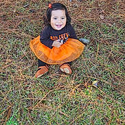 Juliette joined the competition — help win amazing prizes! toddler, child, smiling, orange_tutu, black_shirt, grass, pine_needles, pine_cones, outdoor, nature, happy, sitting, fall, cute, hair_clip, brown_shoes, person, young_child, festive_clothing, joy