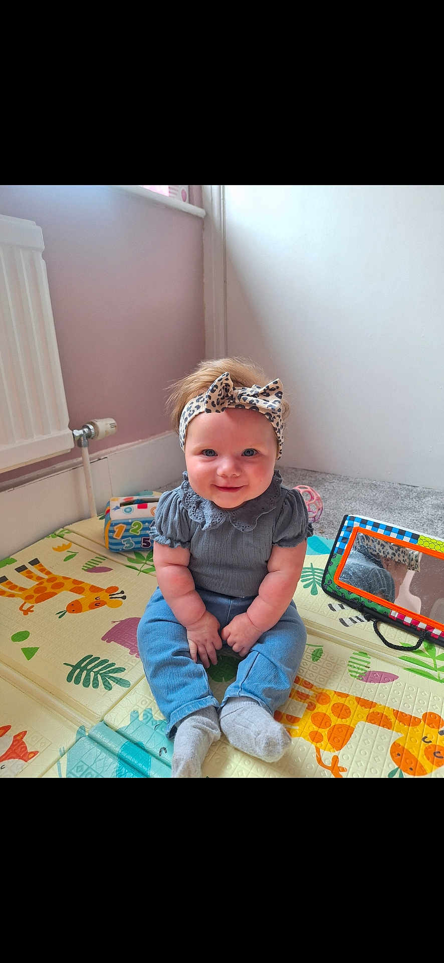 Austeja is registered to the contest to win money with this photo: baby, child, smiling, headband, leopard_print, blue_jeans, gray_shirt, socks, play_mat, giraffe, toy, mirror, indoor, carpet, floor, person, cute, happy, infant, colorful