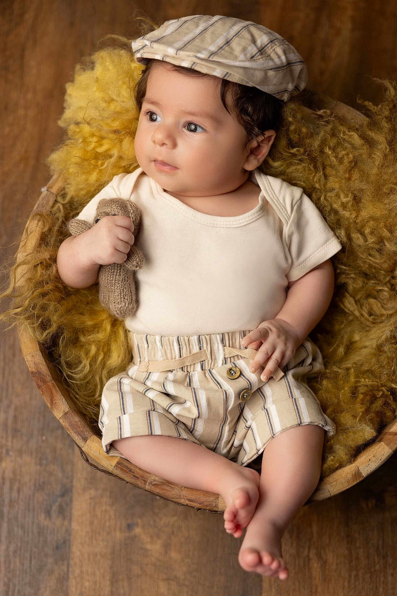 Mateo a rejoint le concours — aidez-le/la à gagner de superbes lots ! baby, infant, child, hat, striped_clothing, knitted_toy, teddy_bear, wooden_bowl, yellow_wool, curious, cute, portrait, indoors, soft_light, plush, relaxing, small_hands, barefoot, cozy, adorable