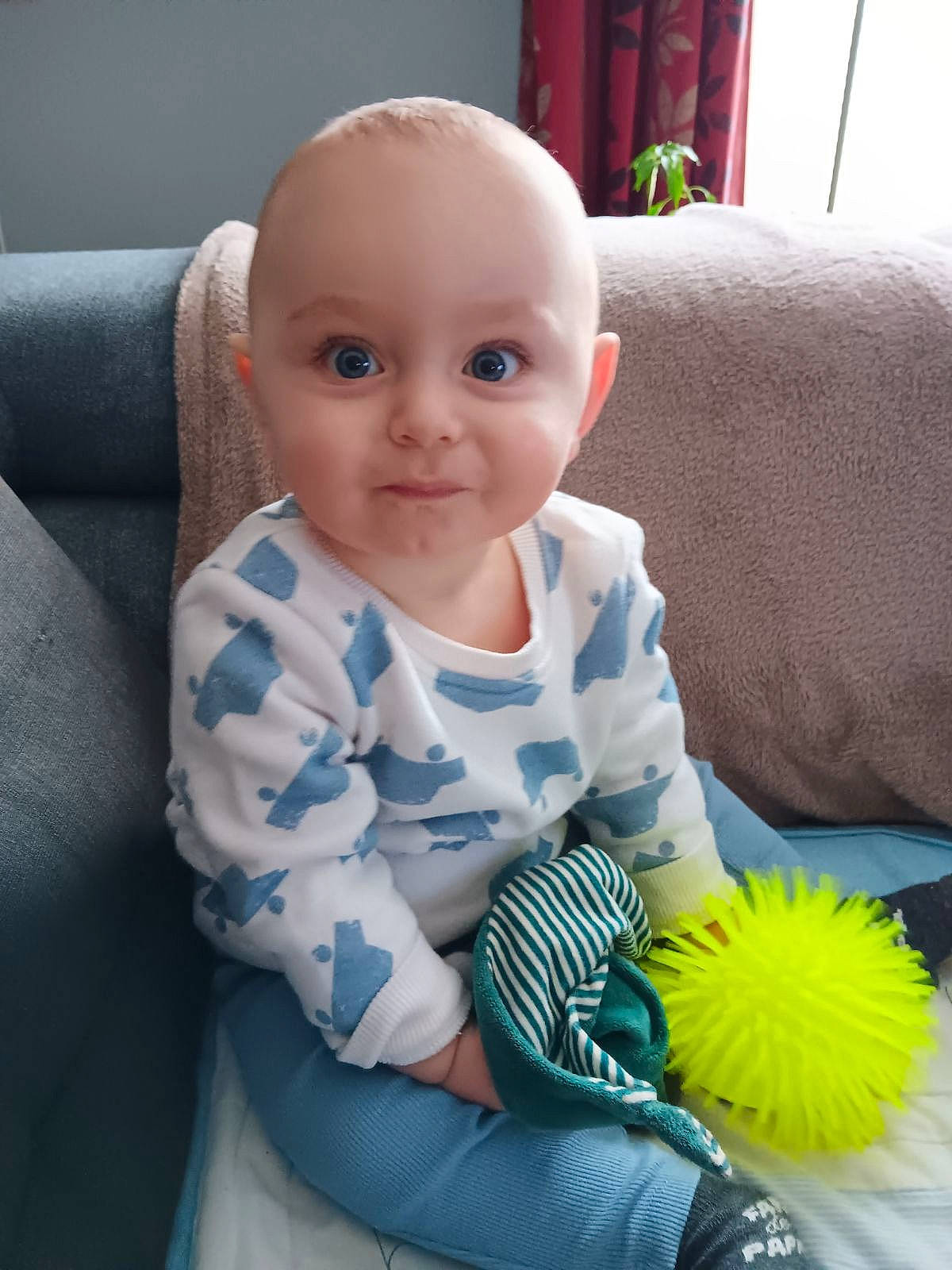 Sacha participe au concours pour gagner de l'argent avec cette photo : baby, baby_products, baby_toddler_clothing, cheek, child, comfort, couch, curtain, electric_blue, happy, iris, joy, linens, person, petal, product, sitting, skin, sleeve, smile