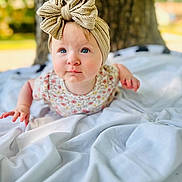 Everleigh joined the competition — help win amazing prizes! baby, child, headband, bow, blue_eyes, blanket, outdoor, tree, nature, portrait, cute, infant, clothing, soft_texture, face, expression, young, toddler, skin, person