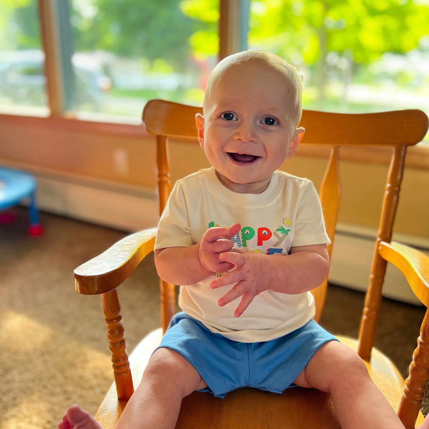 Carson joined the competition — help win amazing prizes! baby, carpet, child, clapping, daylight, feet, furniture, greenery, happy, indoor, legs, person, shorts, sitting, smiling, sunlight, toddler, tshirt, window, wooden_chair