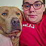 Tank is registered to the contest to win money with this photo: person, dog, glasses, red_shirt, indoor, closeup, face, pet, cuddling, brown_dog, casual, portrait, expression, hand, seated, wall_decor, home, friendship, companion, relaxed
