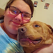 Tank joined the competition — help win amazing prizes! person, dog, glasses, smile, hug, indoor, wall_photos, couch, casual_clothing, brown_dog, closeup, happy, pet, friendship, home, portrait, cozy, affection, face, glasses_reflection
