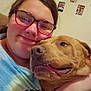 person, dog, glasses, smile, hug, indoor, wall_photos, couch, casual_clothing, brown_dog, closeup, happy, pet, friendship, home, portrait, cozy, affection, face, glasses_reflection
