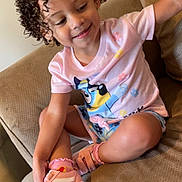 Skylet joined the competition — help win amazing prizes! toddler, child, curly_hair, pink_shirt, shorts, sneakers, socks, couch, indoor, smiling, happy, casual_clothing, seated, cross_legged, cute, playful, person, furniture, home, relaxed