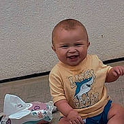 Khaza Dixon joined the competition — help win amazing prizes! baby, child, smiling, yellow_tshirt, shark_graphic, wipes, grass, outdoor, concrete, wall, sitting, happy, toddler, footwear, cute, infant, person, shorts, sock, playful
