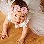 baby, child, girl, crawling, white_dress, headband, flower, pink, wooden_floor, curious, wide_eyes, cute, portrait, indoors, soft_light, closeup, infant, happy, person, toddler