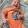 baby, blanket, blue_checkered, cartoon_print, child, clothing, cute, expression, face, hand, happy, indoor, infant, joy, lying_down, mouth_open, orange_shirt, person, smiling, soft_texture
