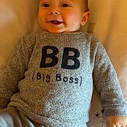 Soan participe au concours pour gagner de l'argent avec cette photo : baby, smiling, sweater, grey_clothing, lying_down, bed, pillow, cute, child, infant, face, hand, text_on_clothing, indoor, soft_lighting, blanket, cozy, happy, person, portrait