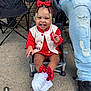toddler, child, smiling, braided_hair, red_bow, beads, white_sneakers, red_socks, chair, concrete, ripped_jeans, adult_leg, outdoor, happy, clothing, person, footwear, casual, portrait, cute