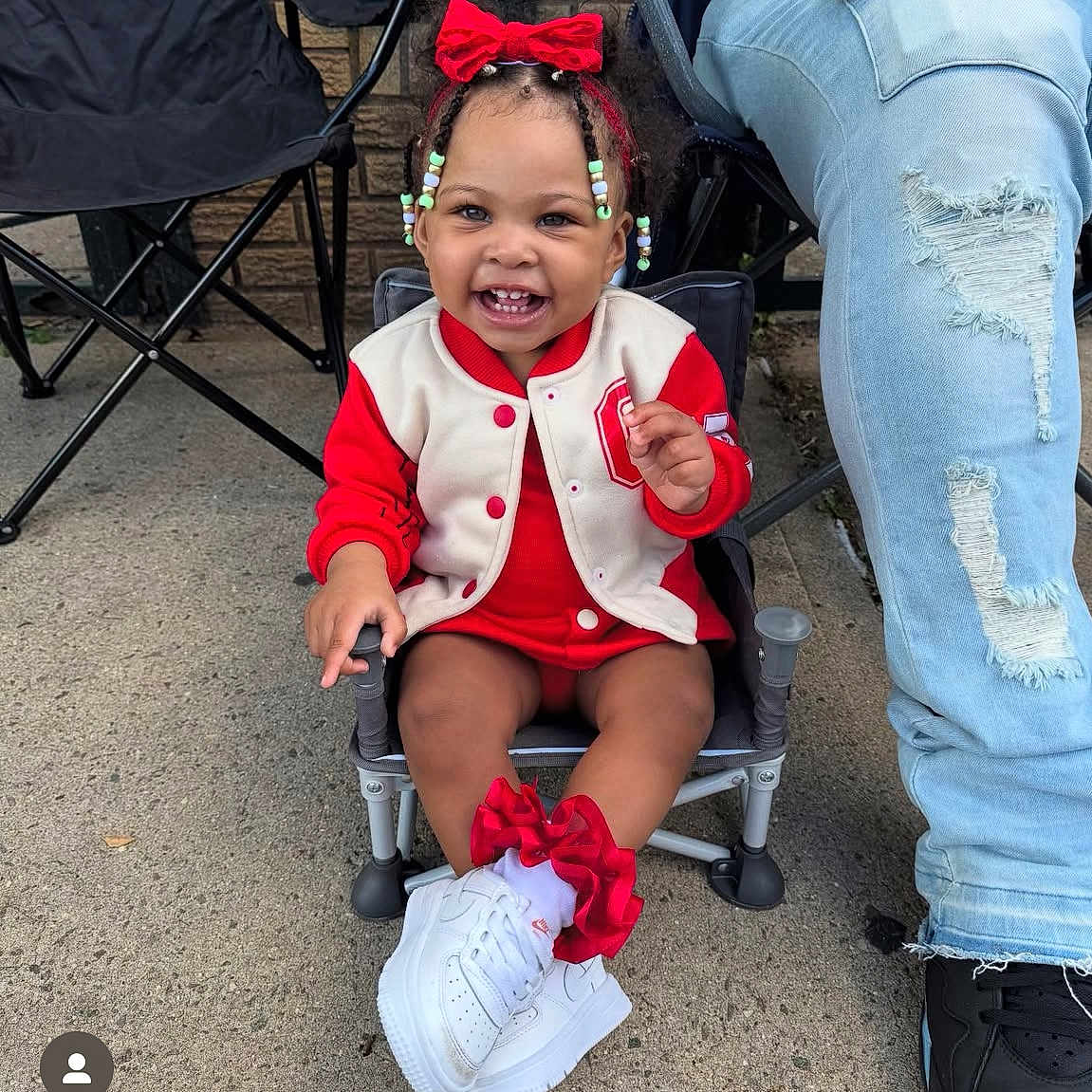 Zaria is registered to the contest to win money with this photo: adult_leg, beads, braided_hair, casual, chair, child, clothing, concrete, cute, footwear, happy, outdoor, person, portrait, red_bow, red_socks, ripped_jeans, smiling, toddler, white_sneakers