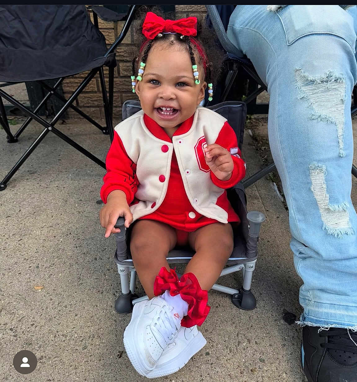Zaria is registered to the contest to win money with this photo: toddler, child, smiling, braided_hair, red_bow, beads, white_sneakers, red_socks, chair, concrete, ripped_jeans, adult_leg, outdoor, happy, clothing, person, footwear, casual, portrait, cute