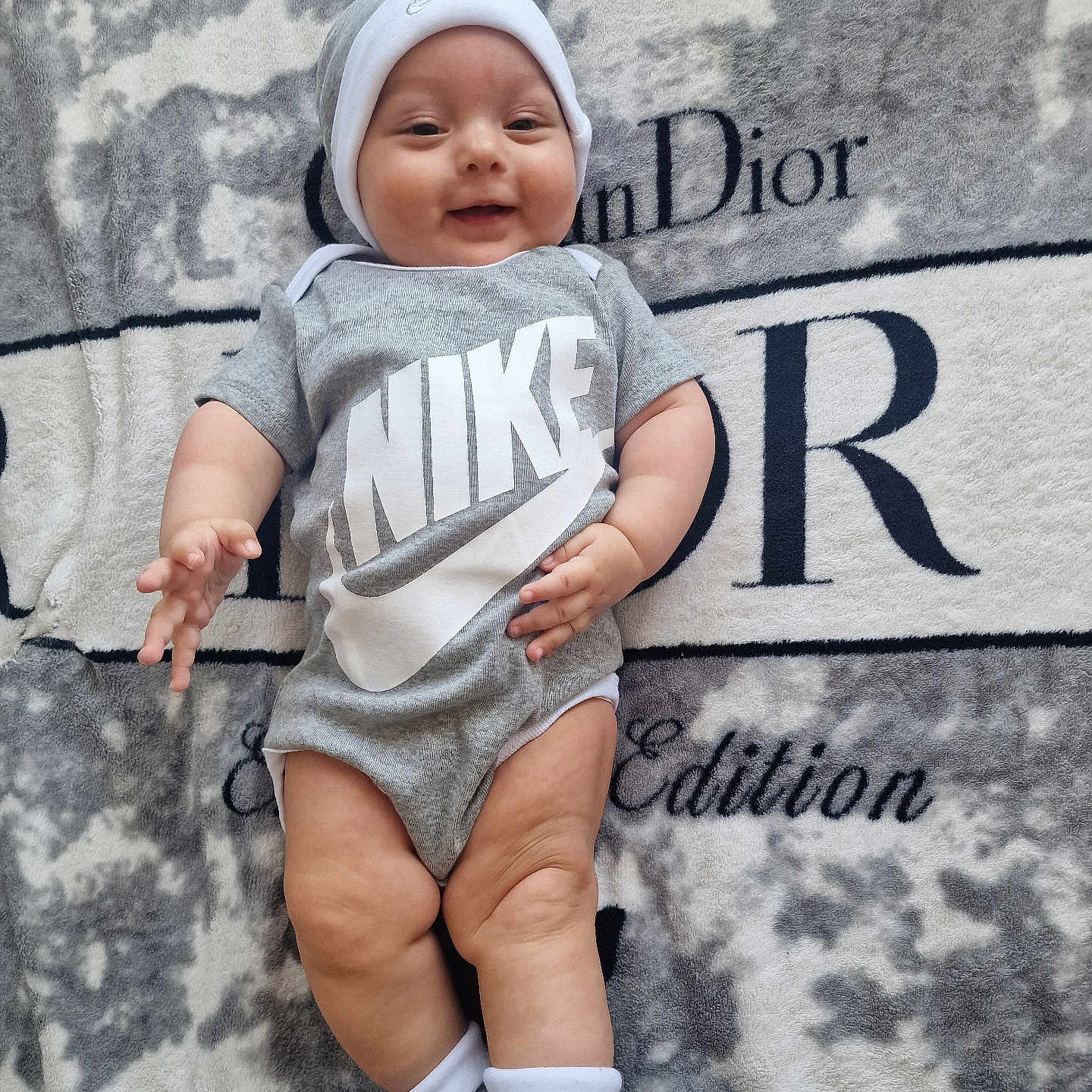 Muna joined the competition — help win amazing prizes! baby, baby_hand, baby_leg, blanket, clothing, cute, dior, happy, hat, indoors, infant, logo, lying_down, nike, onesie, person, portrait, smiling, socks, soft_texture