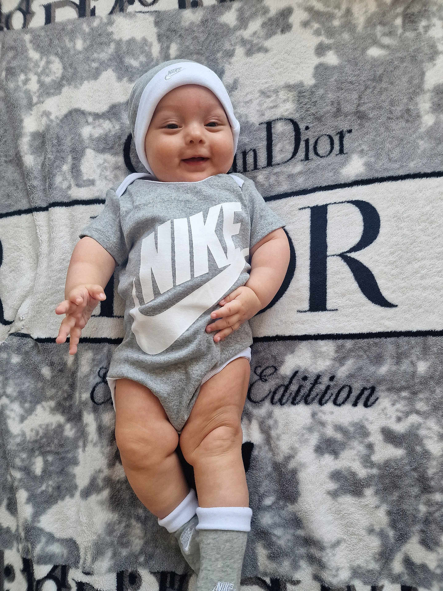 Muna joined the competition — help win amazing prizes! baby, infant, smiling, clothing, onesie, hat, socks, blanket, logo, nike, dior, soft_texture, lying_down, cute, happy, indoors, person, portrait, baby_leg, baby_hand