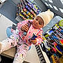 toddler, child, store, counter, candy_bar, snacks, pajamas, beanie, indoor, shopping, convenience_store, shelf, colorful_clothing, cute, person, holding, curious, floor, footwear, toy