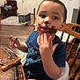 toddler, child, chocolate, face_paint, high_chair, table, bread, food, messy, indoor, wooden_floor, person, furniture, toy, living_room, blue_shirt, hand, smile, cute, young