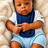 baby, infant, child, curly_hair, blue_bib, white_shirt, blue_shorts, grey_socks, fluffy_blanket, soft_texture, cute, portrait, indoors, comfortable, relaxed, chubby_arms, chubby_legs, looking_at_camera, skin, hands