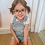 child, girl, glasses, pigtails, smiling, indoor, floor, denim_overalls, white_tshirt, happy, portrait, cute, young, casual_clothing, person, wooden_floor, home, small_child, sitting, playful