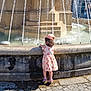 Angelina participe au concours pour gagner de l'argent avec cette photo : child, girl, fountain, water, stone, dress, hat, sandals, outdoor, daylight, curious, back_view, pavement, water_splash, summer, sunlight, urban, public_space, architecture, playful