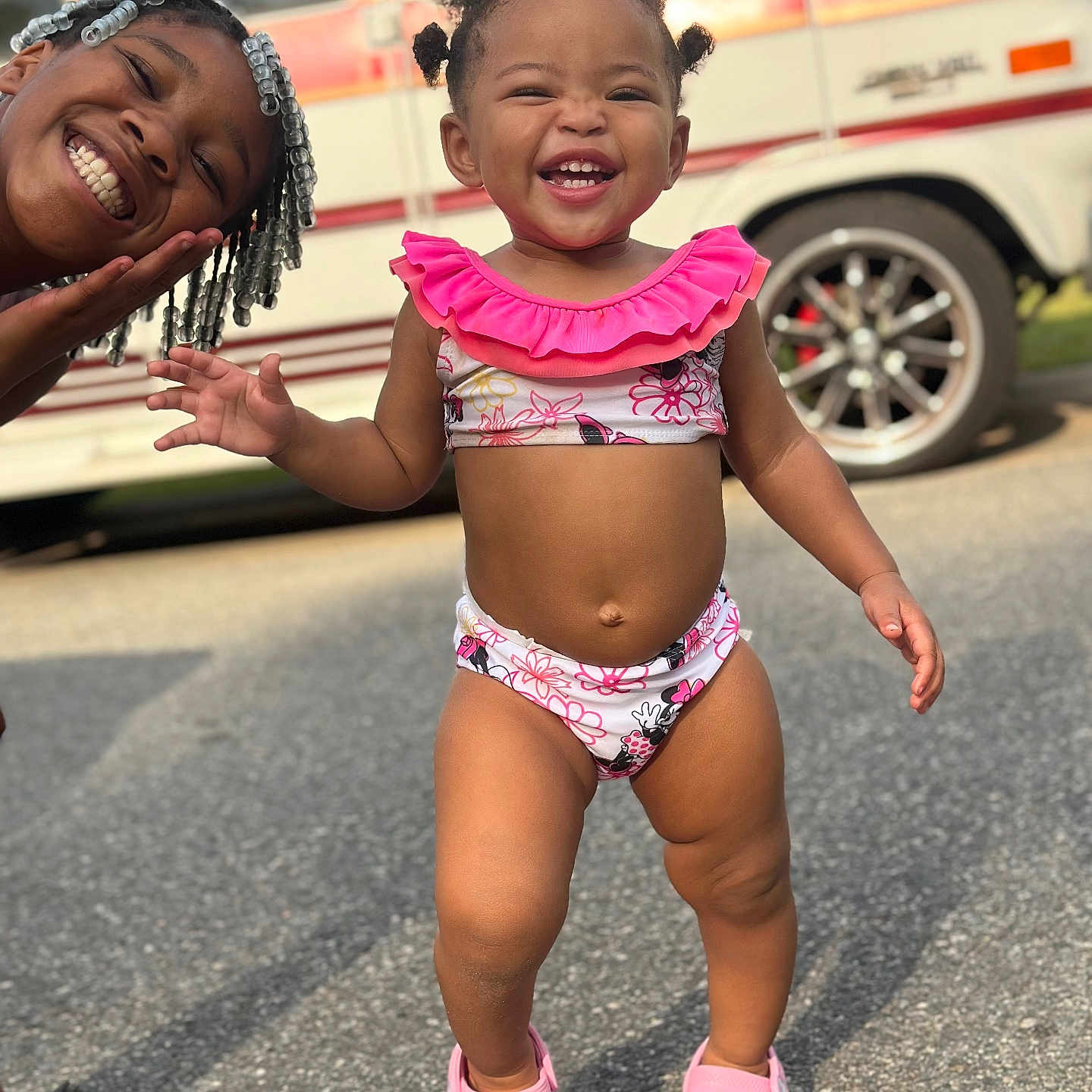 Analeia Hedges joined the competition — help win amazing prizes! beaded_hair, child, cute, footwear, happy, joy, outdoor, pavement, person, pink_shoes, playful, smiling, summer, sunlight, swimsuit, toddler, two_children, van, vehicle, walking