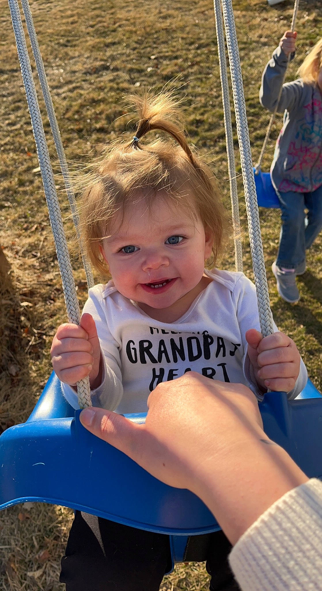 Oaklee is registered to the contest to win money with this photo: arm, blue, clothing, community, facial_expression, fun, grass, hair, hairstyle, happy, joint, leisure, person, photograph, recreation, skin, smile, standing, swing, toddler