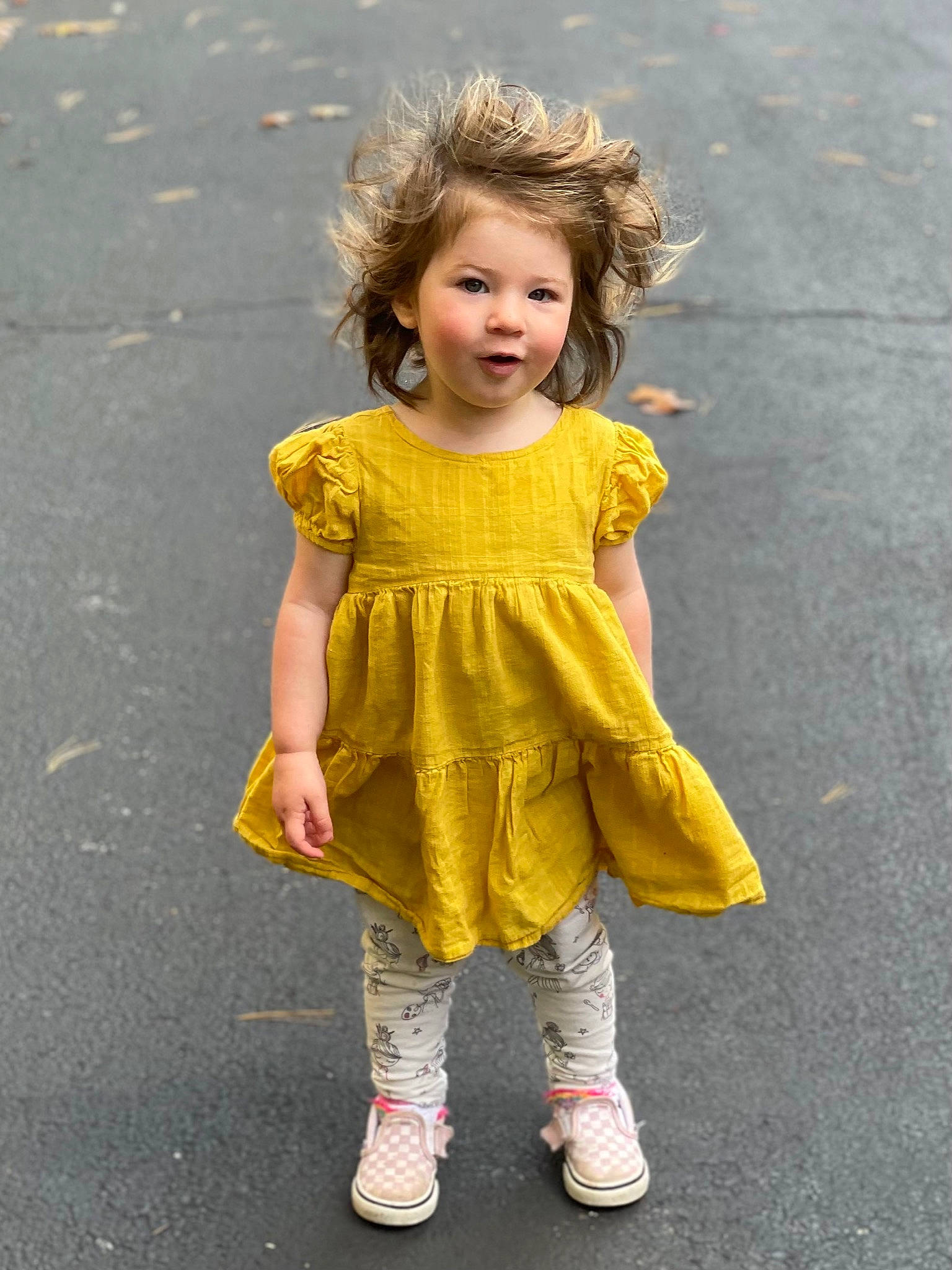 Emmaline is registered to the contest to win money with this photo: asphalt, baby_toddler_clothing, blond, day_dress, dress, face, footwear, fun, grass, hair, happy, human_leg, knee, person, recreation, road_surface, sleeve, standing, street_fashion, toddler