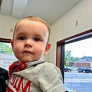 Elliot joined the competition — help win amazing prizes! toddler, child, indoor, window, face, person, shirt, short_sleeve, red, grey, car, vehicle, street, plant, pot, building, curious, calm, natural_light, portrait