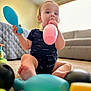 Elliot is registered to the contest to win money with this photo: baby, child, indoor, carpet, toy, balloon, blue_toy, pink_balloon, sitting, living_room, couch, curious, infant, clothing, floor, playtime, person, cute, colorful, young