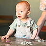 baby, child, toddler, portrait, indoor, standing, striped_shirt, overalls, curious, face, eyes, mouth, table, snacks, food, adult, background, warm_lighting, closeup, photography