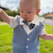 Atticus is registered to the contest to win money with this photo: baby, child, outdoor, portrait, face, bow_tie, vest, dress_shirt, plaid, formalwear, blond_hair, blue_clothing, standing, arms_raised, grass, garden, sunlight, blurred_background, smiling, fashion