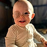 Atticus is registered to the contest to win money with this photo: baby, child, infant, smiling, portrait, close_up, eyepatch, medical_patch, face, eyes, teeth, sitting, onesie, clothing, indoor, warm_lighting, sunlight, blurred_background, happy, adorable