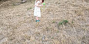 Maialen a rejoint le concours — aidez-le/la à gagner de superbes lots ! brown, casual, child, curious, daylight, dry_grass, exploration, field, girl, green, isolated, long_hair, nature, outdoor, play, standing, summer, trees, white_dress, young_person
