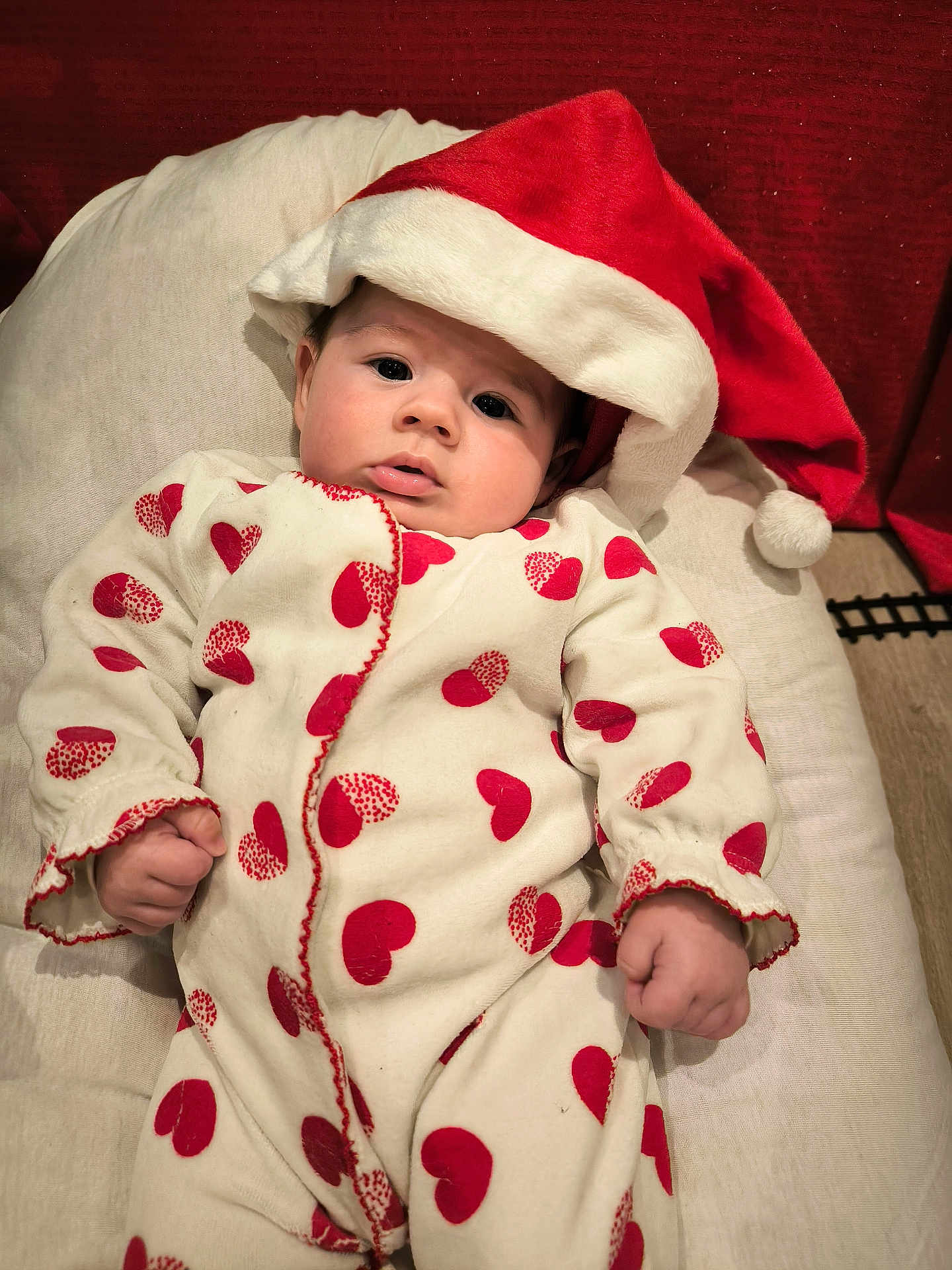 Alba participe au concours pour gagner de l'argent avec cette photo : baby, infant, santa_hat, onesie, red_hearts, cushion, soft_toy, holiday, festive, cute, portrait, indoor, child, face, clothing, cozy, smile, holiday_season, young, celebration