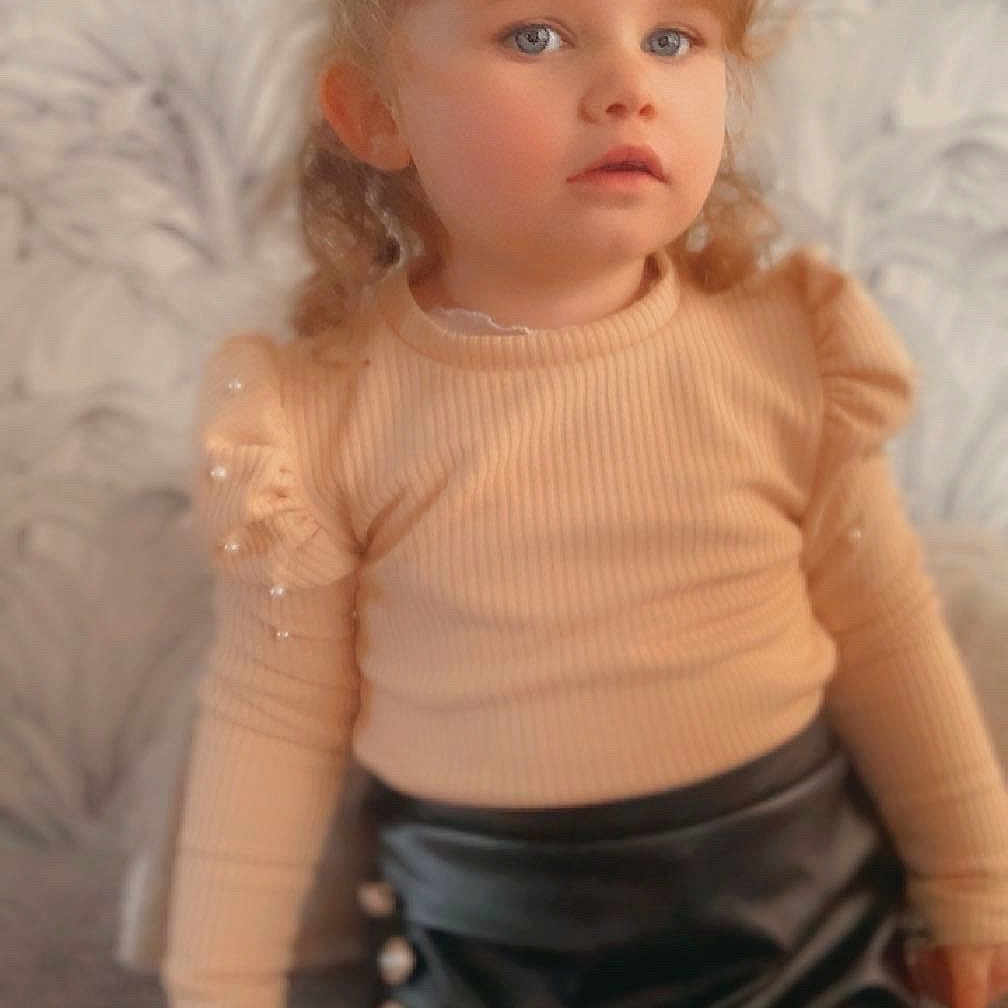 Lya a rejoint le concours — aidez-le/la à gagner de superbes lots ! child, girl, portrait, curly_hair, blue_eyes, beige_top, black_skirt, buttons, indoor, soft_lighting, fashion, cute, young, person, toddler, background_pattern, long_sleeves, expression, standing, photography