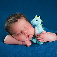 Elliott is registered to the contest to win money with this photo: baby, sleeping, plushie, dinosaur, soft_toy, blue, blanket, cozy, infant, cute, child, peaceful, resting, portrait, closeup, hand, face, skin, hair, indoor