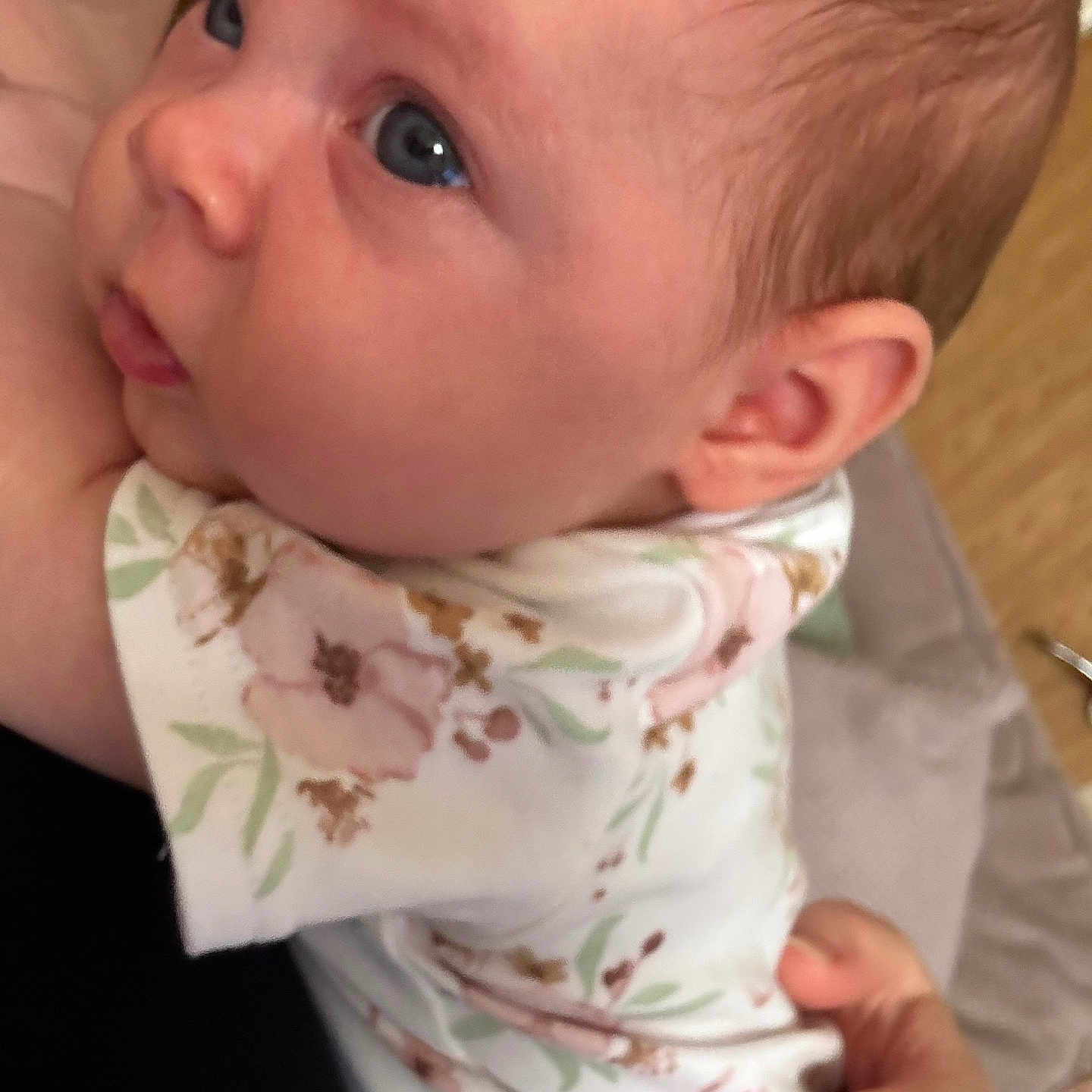 Amelia is registered to the contest to win money with this photo: baby, blue_eyes, caring, child, close_up, curious, face, floral_clothing, hand, head, holding, human, indoor, infant, onesie, person, portrait, skin, soft_light, young